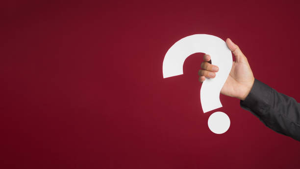 istock Hand of a woman in a black shirt holding a white question mark paper while standing on a red background. 1485648311