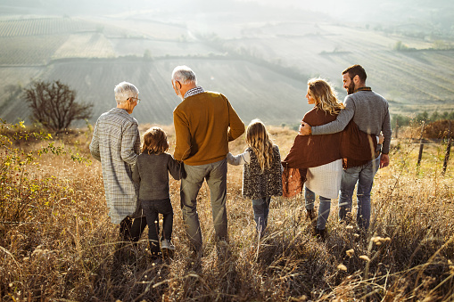 Rear view of happy multi-generation family holding hands and talking while going down the hill.
