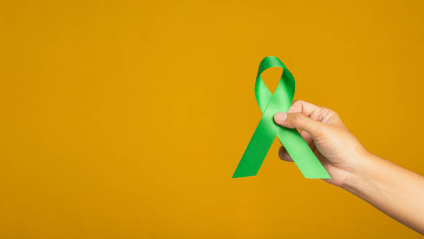 istock Hand holding of a green ribbon over on a yellow background. 1485649437