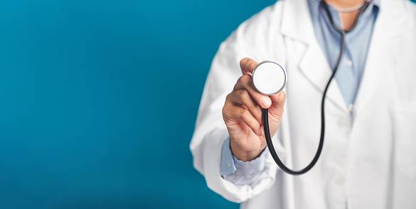 Hand of a doctor holding a stethoscope while standing on a blue background. Close-up photo. Space for text. Medical, treatment, and healthcare concept.