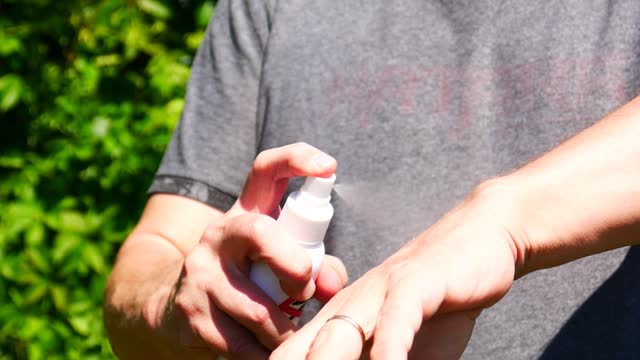 Close-up of the hands of a man spraying himself with anti mosquito spray