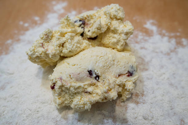 Stock photo showing close-up view of a cake stand containing a golden, fruit scone, with  filled with clotted cream and strawberry jam. The scone is filled in the Cornish way with jam spread on the scone first, followed by a dollop of clotted cream.