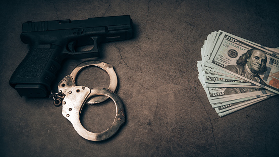 A police officer's pistol and handcuffs lies on a black background, lots of dollars, bribery police, corrupt police.
