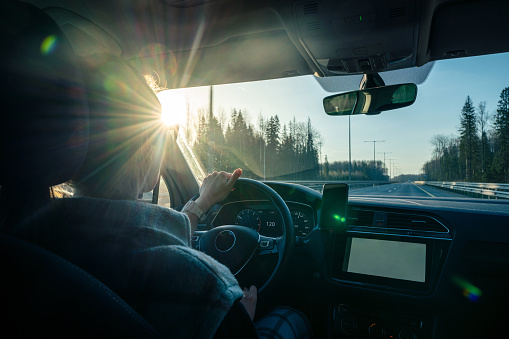 Woman driving car at highway at sunset. View from the back passenger seat