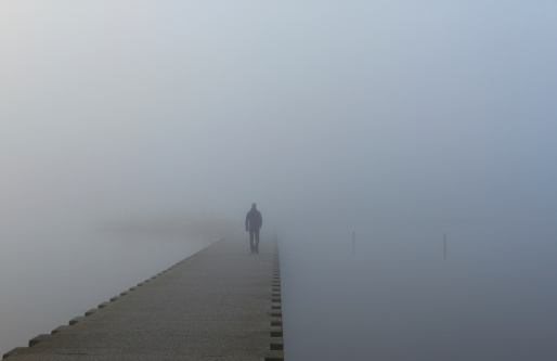 Man on a jetty walking into the dense fog.