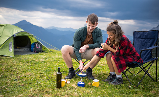 Outdoor camping adventure, preparing a meal in the mountains and enjoying a beautiful day in nature. Healthy lifestyle and simple living concept.