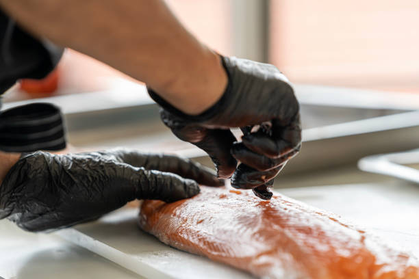 Chef preparing a fresh salmon fillet in Japanese kitchen. Close up hand of chef Pulling salmon fish bone for making sashimi. stock photo