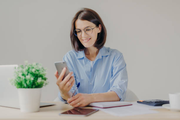 istock Pretty successful talented female copywriter blogs on smart phone, works on laptop computer, checks notification on modern electronic gadget, writes something in notebook with pen. Technology, job 1485674439