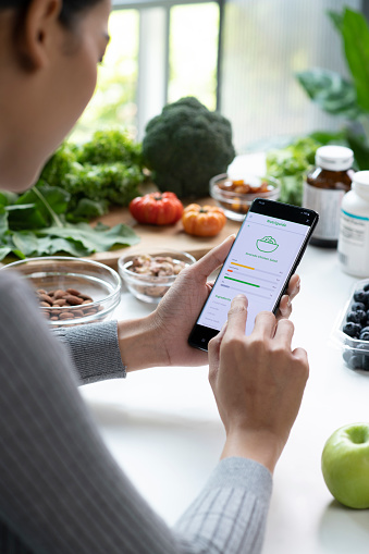 Woman Asian Professional Nutritionist busy working and checking data from a phone with a variety of fruits, nuts, vegetables, and dietary supplements on the table