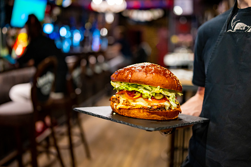 waiter hands hold a plate with a very big cheeseburger in pub