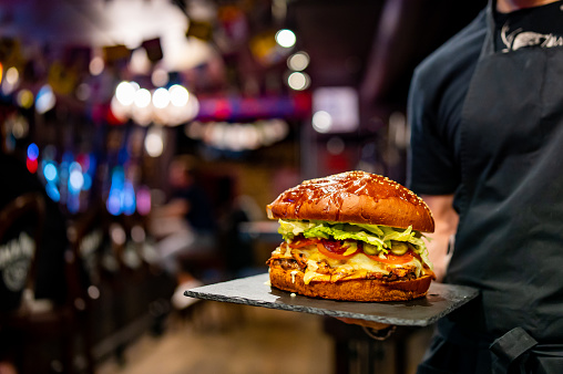 waiter hands hold a plate with a very big cheeseburger in pub