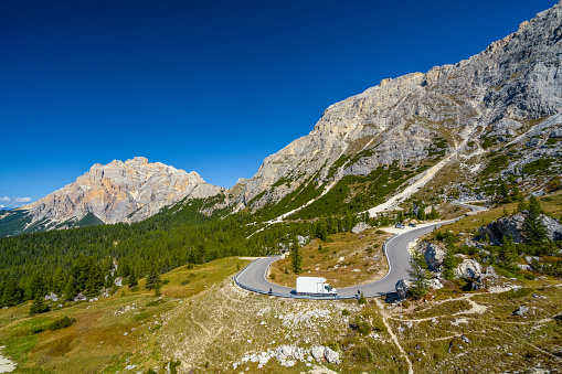 White truck on his was up curvy mountain pass road high up in the dolomites on sunny day with clear blue sky