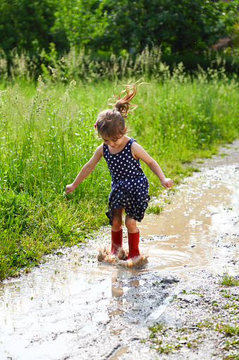 Little girl jumping in puddle in rubber boots.