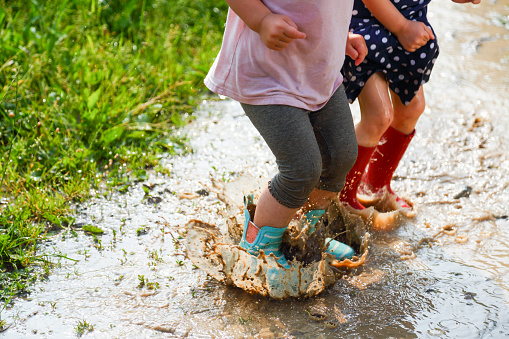 Girls walking, running and jumping on mud puddles in their rubber boots. Having fun.