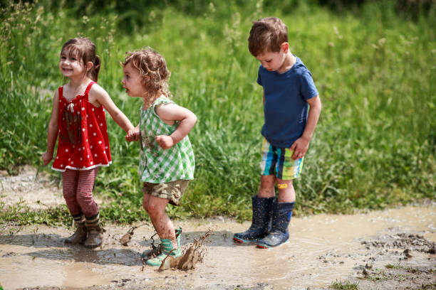Children jumping in puddles of mudd Little boy and two little girls jumping on mud puddles on a nice summer day. kids dirty shoes stock pictures, royalty-free photos & images