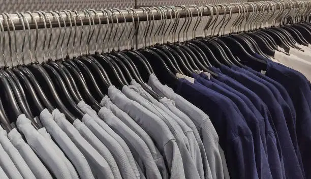 Row of Grey blue T-Shrit in store,Unisex dresses on steel hangers in a retail shop