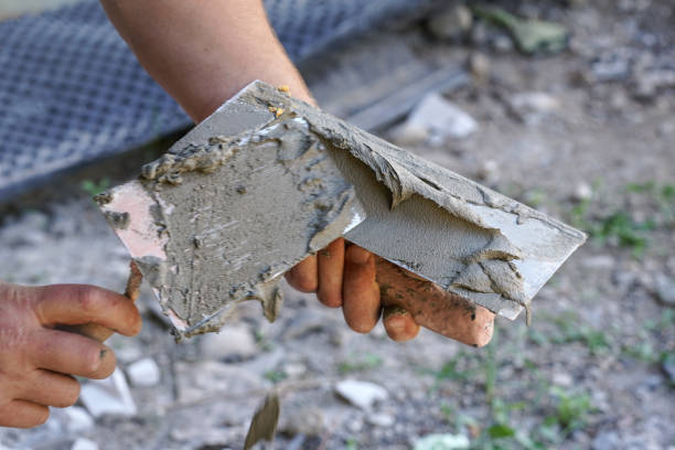 Man putting wet paste cement mortar mix on masonry trowel with metal spattle, one hand blurred to emphasise action, closeup detail