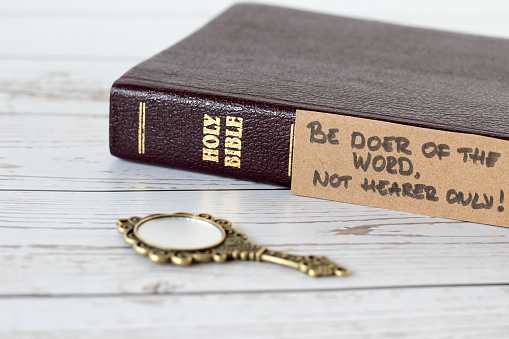 Be doer of the Word, not hearer only, handwritten verse with closed holy bible book and antique golden mirror on wood. A closeup. James 1:22 Scripture, obedience to God Jesus Christ, Christian concept.