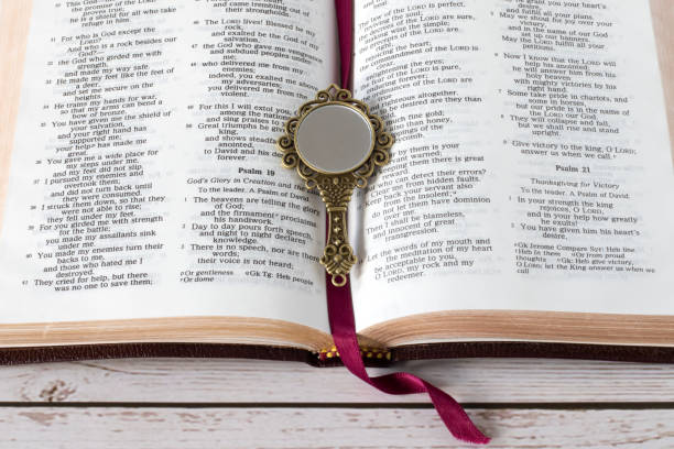 istock Open holy bible book and antique mirror on wooden table, top view 1485690835