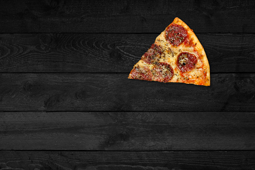 Close up view of pork pizza isolated on black wooden table.