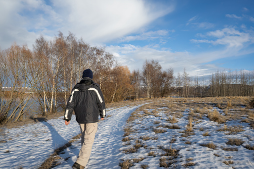 Young boy wearing warm winter clothing walking through field of snow. It is a grey overcast day