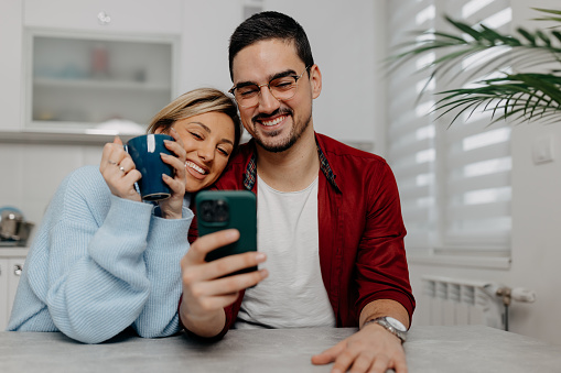 A young Caucasian couple is shopping online together from their kitchen.