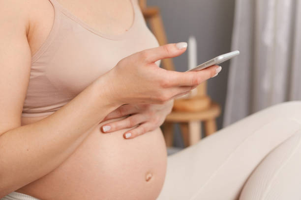 istock Unrecognizable pregnant woman sitting in bed wearing beige top using mobile phone typing messages browsing internet, holding smart phone. 1485702665