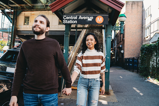 A millennial couple is exiting from the elevated train station in Bushwick, Brooklyn. They are hanging out together, holding hands.