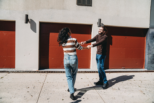 An hipster couple is dancing together on the sidewalk in Brooklyn. They are having fun together in the city.