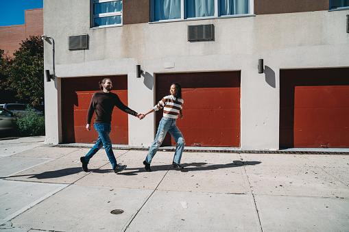 An hipster couple is running together on the sidewalk in Brooklyn. They are having fun together in the city.