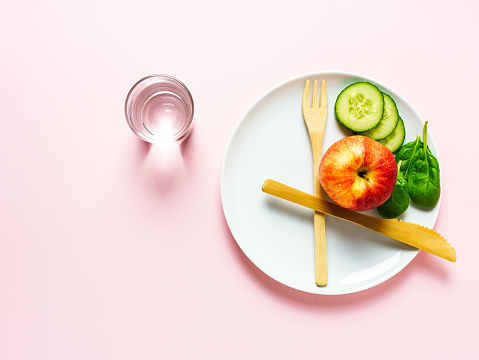 Intermittent fasting, cutlery, 8/16, apple, cucumber, break, pink background, water, drinking glass, overhead view