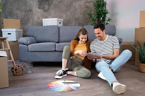 The young Caucasian couple, sitting on the floor looking at a paint color swatch, while planning a renovation in their new apartment