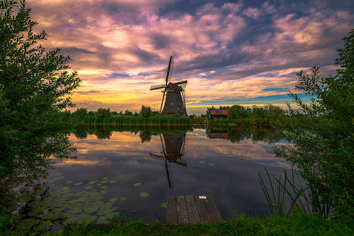 Colorful sunset above old dutch windmill and a river flowing by in Kinderdijk, Netherlands.