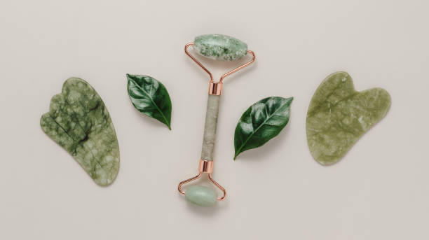 istock Jade face roller and gua sha stone massager with green leaves on pastel background 1485712373