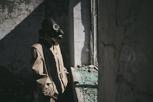 a person wearing a gas mask is standing in front of the window of a destroyed house, good for book cover
