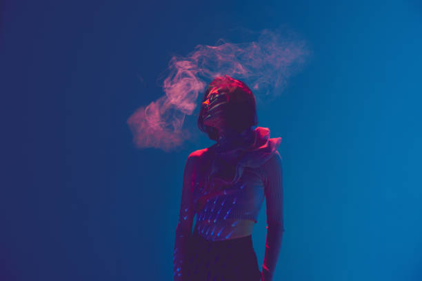 портрет красивой грустной женщины, девушки, использующей вейп, электронную сигарету на синем фоне в неоновом свете. никотиновый наркоман - futuristic reflection fashion women стоковые фото и изображения