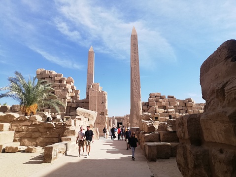 The travel tour group wanders through Karnak Temple. Egyptian landmark with hieroglyphics, decayed temples, obelisks, towers, and other buildings.