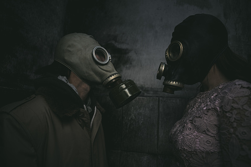 two people in gas masks stand against a wall in a small dark room and look at each other, closeup, good for book cover