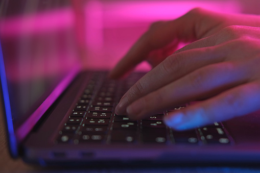 Person typing at laptop computer at night. Female uses keyboard, shakes buttons with fingers. Internet security, cyber attack. Trendy neon light. Creative vivid color of ultraviolet red and blue. 4K. pink and blue illumination. blog content. cyberspace, sale shop, delinquency concept. data theft, data protection. mobility. wifi. easy pay