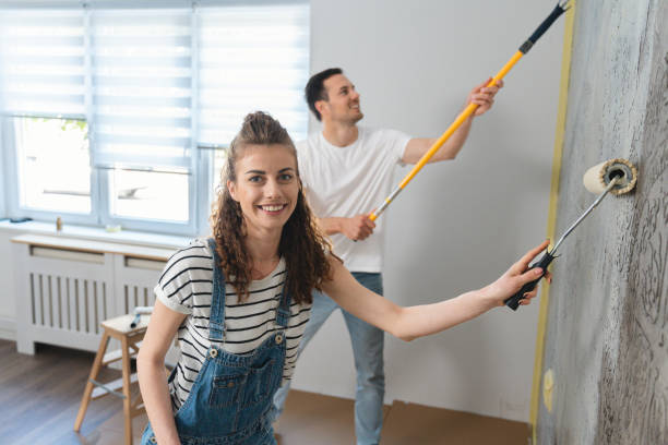 pareja caucásica pintando la pared de su nuevo apartamento - home improvement couple painting real estate fotografías e imágenes de stock