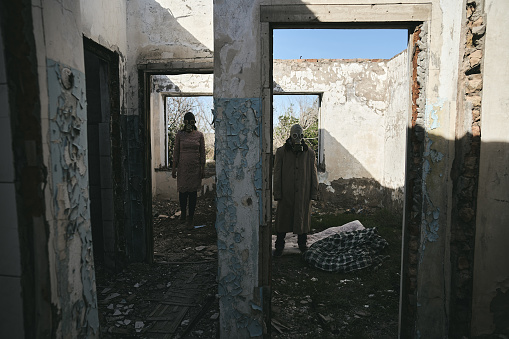 A man and a woman in a destroyed building, with gas masks, stand in different rooms, good for book cover