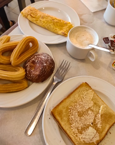 Toast with butter, churros, omelette (egg, flour, cheese and ham), cake and coffee with milk