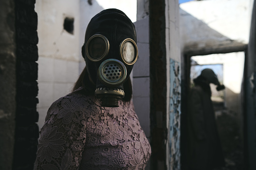 the woman in a gas mask staying in front of a man in destroyed building, good for book cover