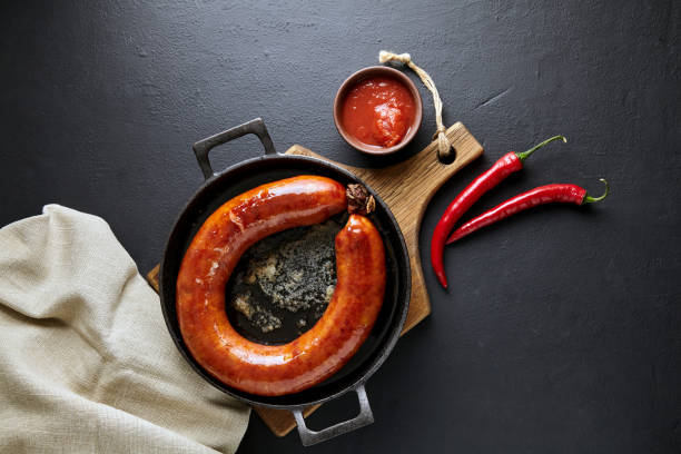 istock Grilled sausage rolled into a ring in a cast iron pan with pepper and ketchup on a black stone background 1485729737