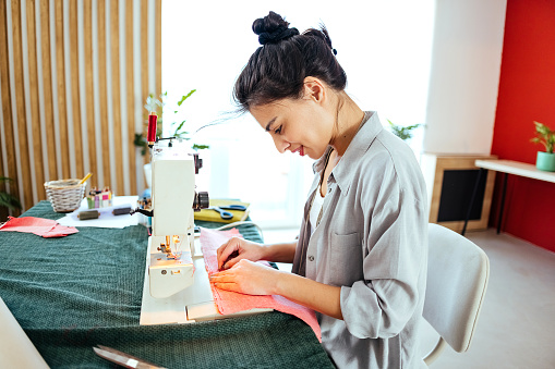 Woman sits at a table and works with a sewing machine.