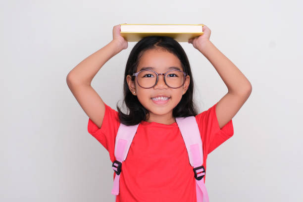 istock Asian kid wearing school bag putting a book above her head with happy expression 1485732169