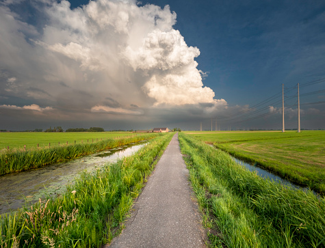 Long straight road through a scenic field with a storm cloud on the horizon.
