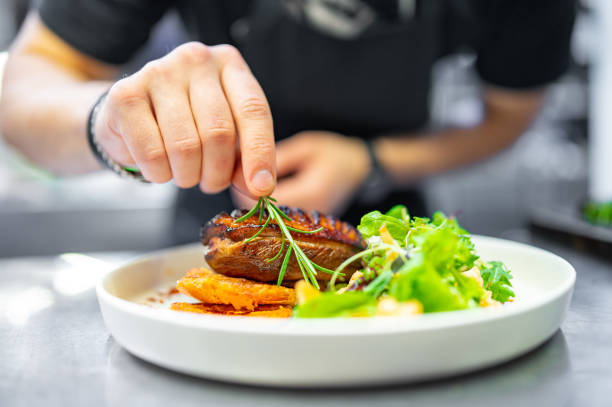 chef cuisinier à la main Filets de magret de canard rôti avec salade de légumes et batat dans l’assiette sur la cuisine du restaurant - Photo