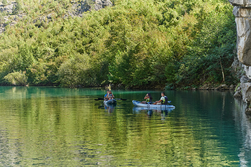 A group of friends enjoying fun and kayaking exploring the calm river, surrounding forest and large natural river canyons during an idyllic sunset