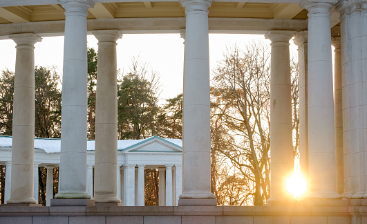 beautiful setting sun shines through the old columns in the park on a winter evening